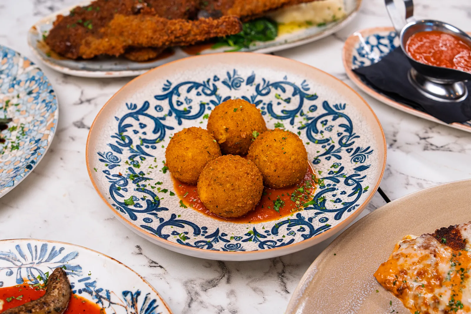 Four golden fried arancini on a bed of tomato sauce on a blue and white plate