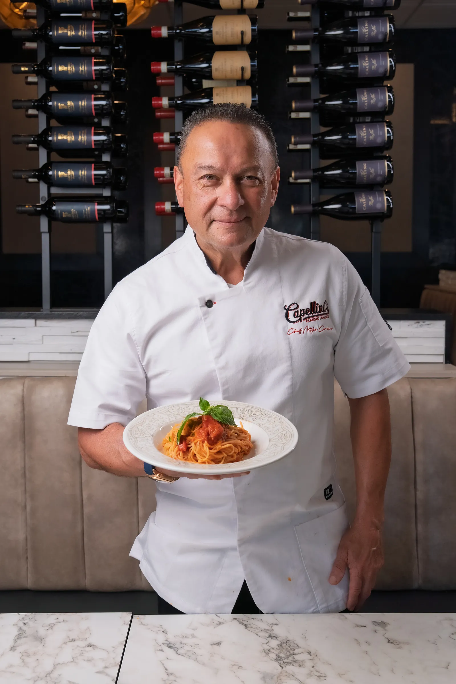 Chef Mike Cordero standing in his Capellini's chef jacket, holding a plate of spaghetti pomodoro