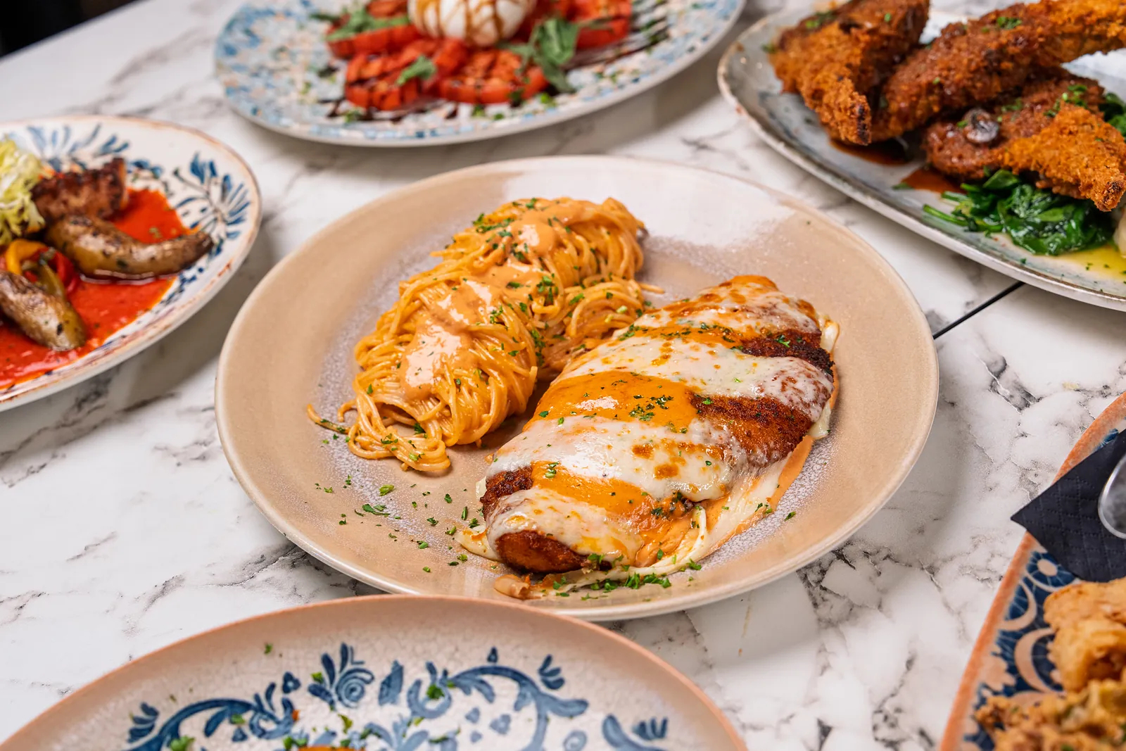 Breaded chicken cutlet under melted mozzarella and sauce, served with a nest of spaghetti on a cream plate